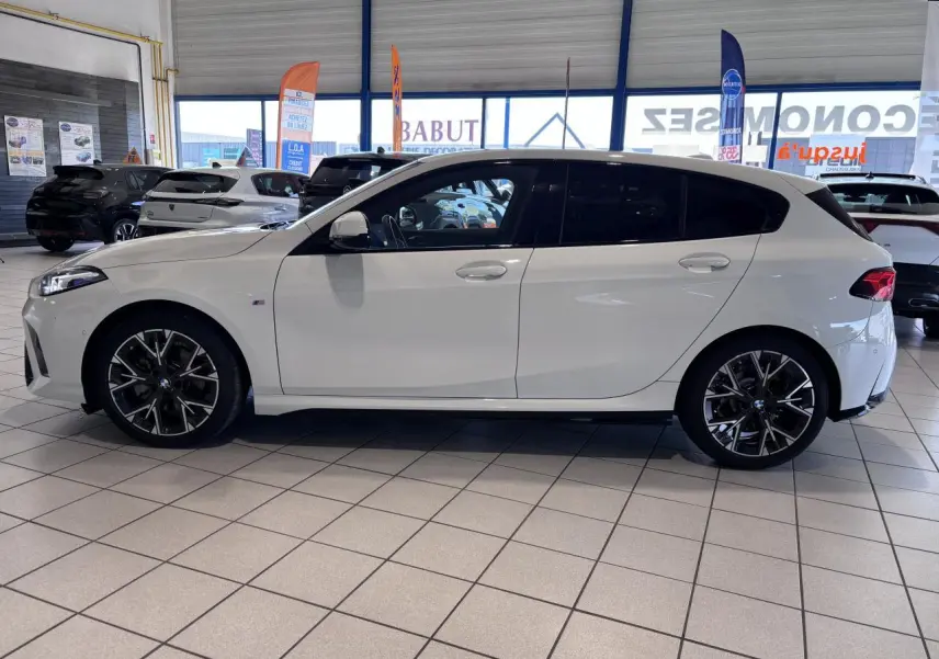 BMW Série 1 120d M Sport blanc vue de profil côté gauche, avec jantes noires et vitres teintées, en showroom.