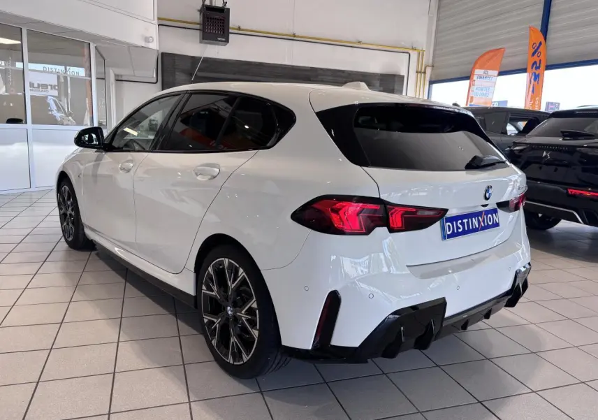 Vue 3/4 arrière droite d'une BMW Série 1 120d M Sport blanche avec jantes noires en concession.
