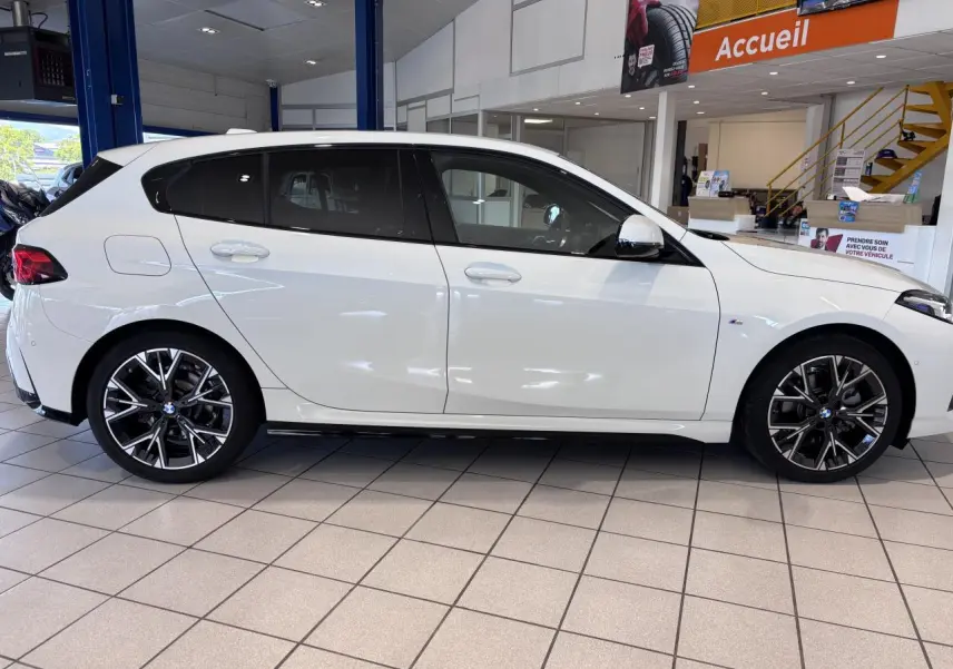 BMW Série 1 120d M Sport blanche vue de profil côté gauche en intérieur, avec jantes alliage distinctives.