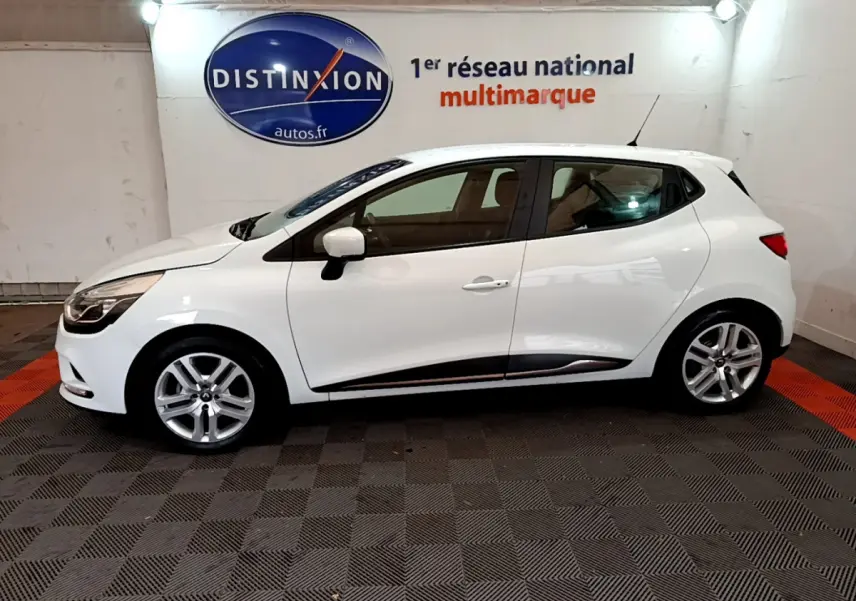 Profil droit d'une Renault Clio Business TCe 90 blanche, avec jantes alliage et logo Distinxion en arrière-plan.