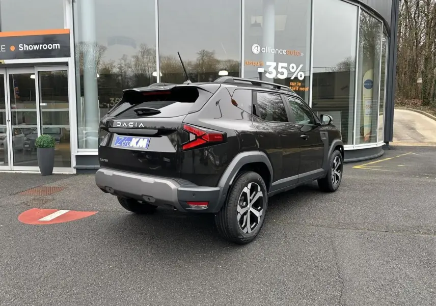 Vue 3/4 arrière droite du Dacia Duster noir métallisé 2025 avec jantes alliage 18” et barres de toit longitudinales.
