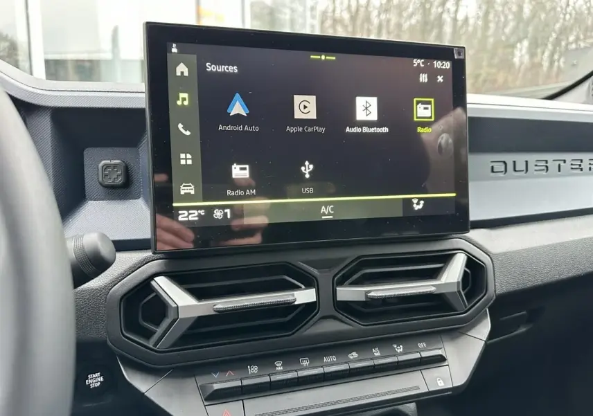 Vue intérieure du tableau de bord du Dacia Duster 2025 noir, avec écran tactile central et aérateurs hexagonaux.