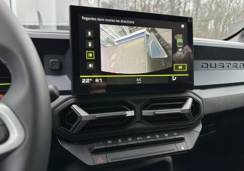 Vue intérieure du tableau de bord du Dacia Duster noir 2025, écran tactile affichant la caméra de recul et aérateurs hexagonaux.