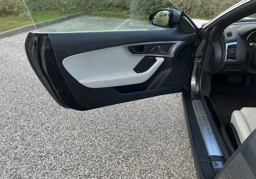 Vue intérieure côté gauche de la porte ouverte d'une Jaguar F-TYPE II Coupé grise avec garniture cuir claire et seuil métallique Jaguar.