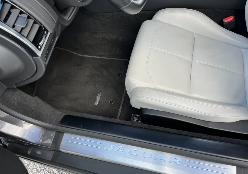 Vue intérieure côté conducteur d'une Jaguar F-TYPE gris Corris, avec siège cuir clair et seuil de porte métallique Jaguar.