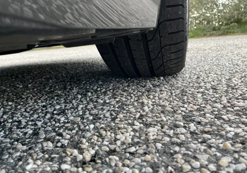 Gros plan sur le pneu arrière droit d'une Jaguar F-TYPE II Coupé 2.0T 300 BVA8 gris Corris, sur sol gravillonné.