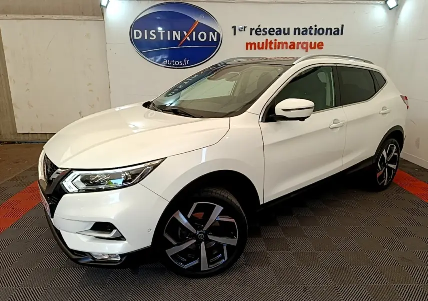 Nissan Qashqai blanc en 3/4 avant droit, avec jantes alliage noires et toit vitré visible en intérieur showroom.