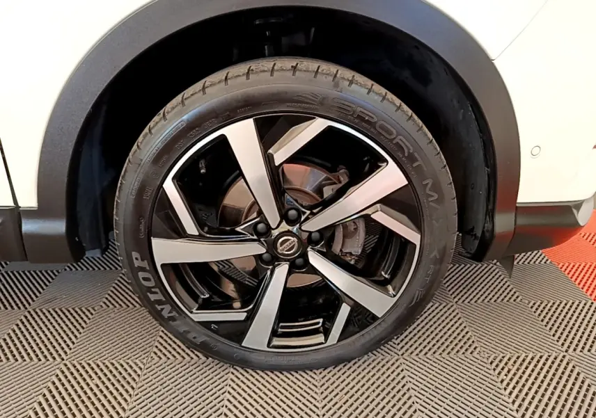 Gros plan sur la roue arrière droite d’un Nissan Qashqai blanc, mettant en valeur la jante alliage noire et argent.