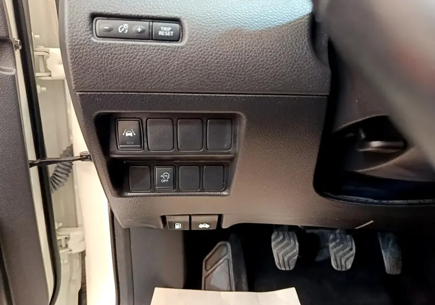 Détail intérieur côté gauche du tableau de bord noir avec commandes et pédales du Nissan Qashqai blanc 2019.