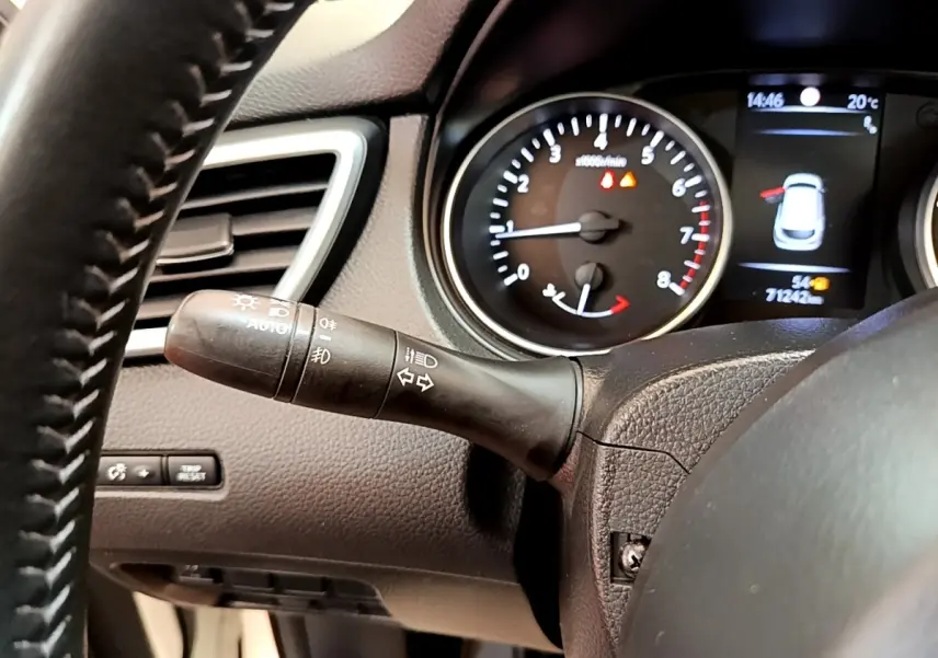Gros plan sur le commodo gauche du tableau de bord noir du Nissan Qashqai blanc, avec compte-tours et écran multifonction.