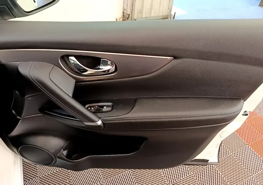 Gros plan sur la porte avant droite noire du Nissan Qashqai blanc, avec poignée chromée et commandes de vitres.