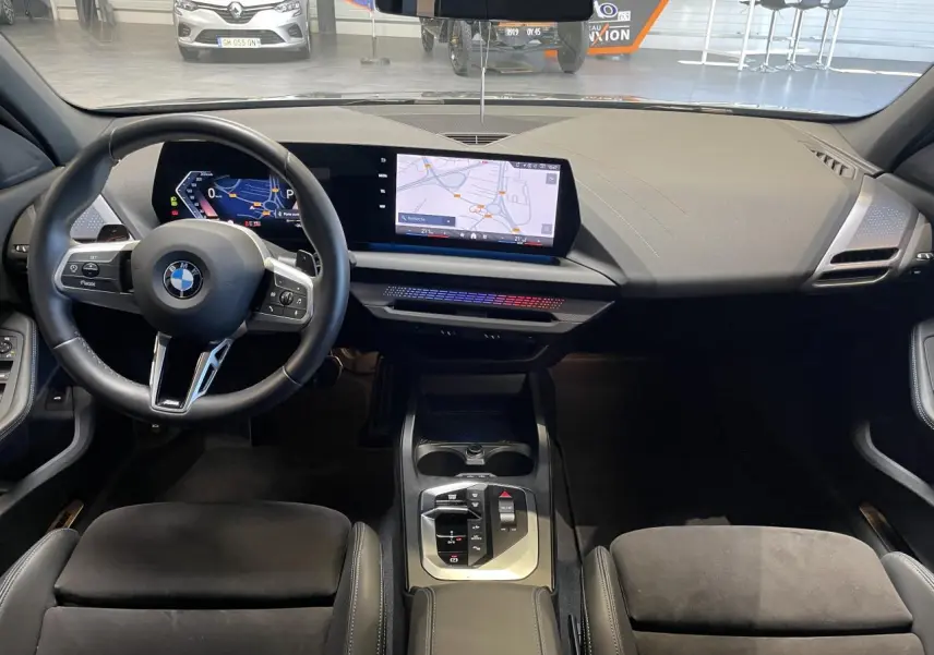 Vue intérieure avant de la BMW Série 1 120d M Sport 2025, tableau de bord moderne avec écran tactile et volant multifonction noir.