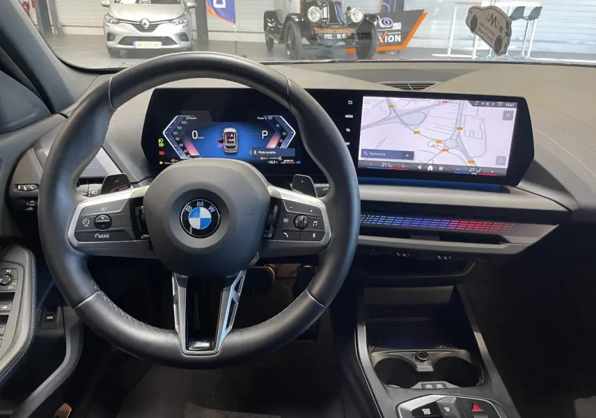 Vue intérieure centrée sur le volant BMW M Sport et le tableau de bord numérique avec écran tactile de la Série 1 gris 2025.