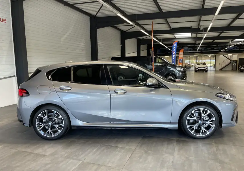 BMW Série 1 120d M Sport gris vue de profil côté gauche dans un showroom lumineux avec jantes sport.