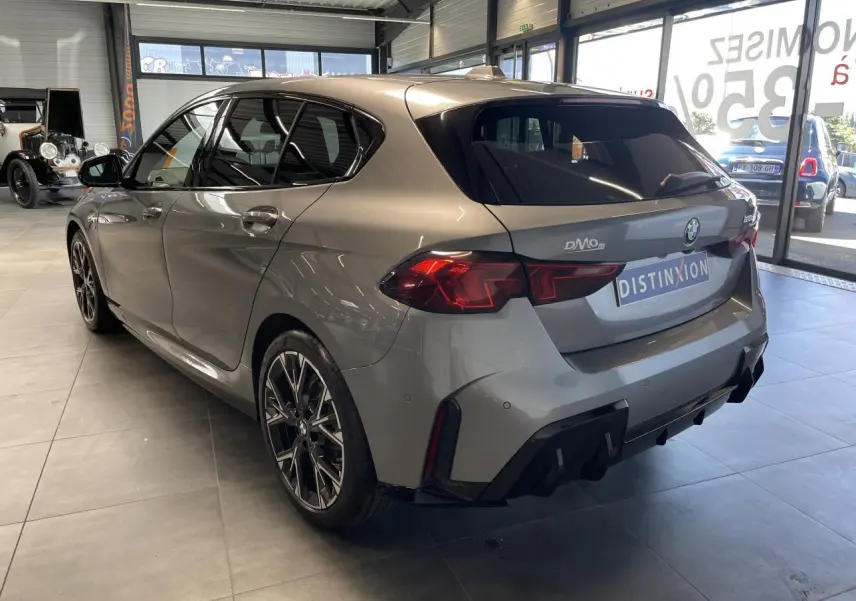BMW Série 1 120d M Sport gris vue 3/4 arrière droit en intérieur, avec jantes sport et feux arrière LED distinctifs.