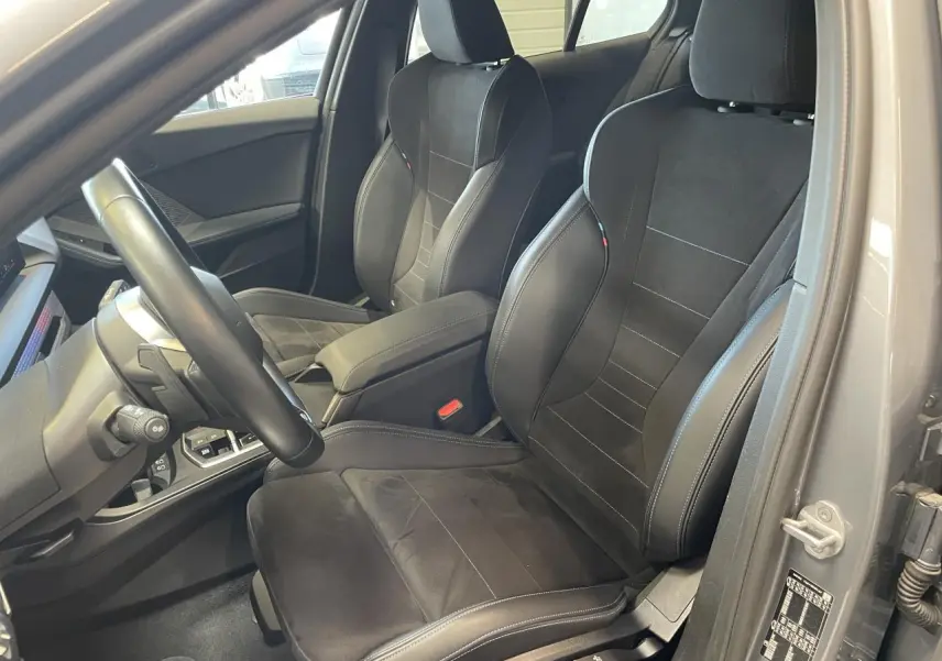Intérieur de la BMW Série 1 120d M Sport 2025, vue côté conducteur, sièges sport noirs avec surpiqûres contrastées.