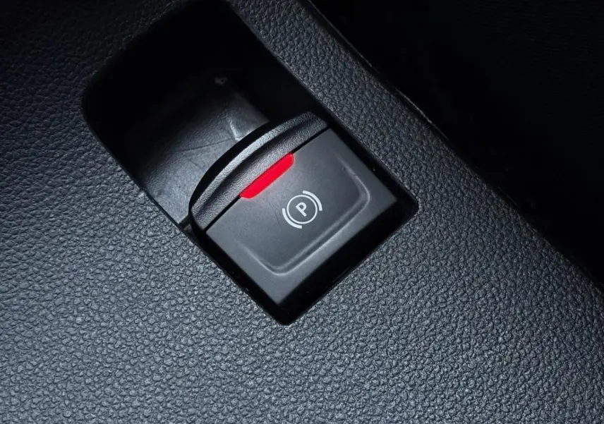 Gros plan sur le bouton de frein de parking électrique avec témoin rouge dans l'habitacle noir du Dacia Sandero Stepway 2025.
