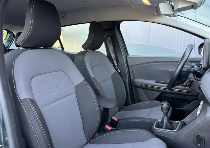 Vue intérieure côté conducteur de la Dacia Sandero Stepway 2025, sièges gris et noir avec accoudoir central.