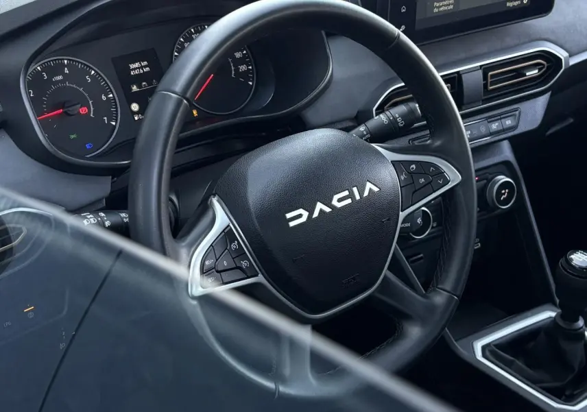 Vue rapprochée du volant noir Dacia et du tableau de bord avec écran tactile sur la console centrale d'une Sandero Stepway 2025.