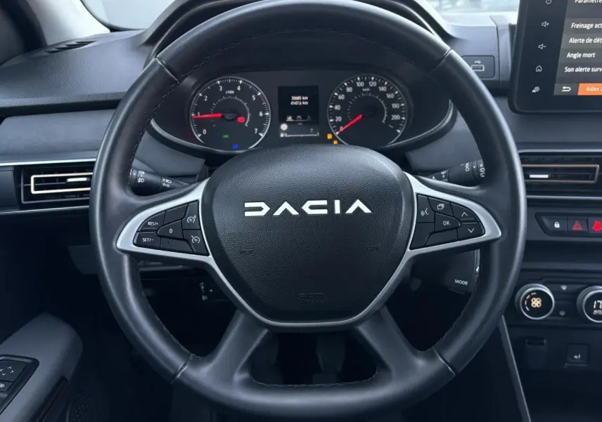 Vue rapprochée du volant noir de la Dacia Sandero Stepway 2025 avec commandes intégrées et tableau de bord numérique.