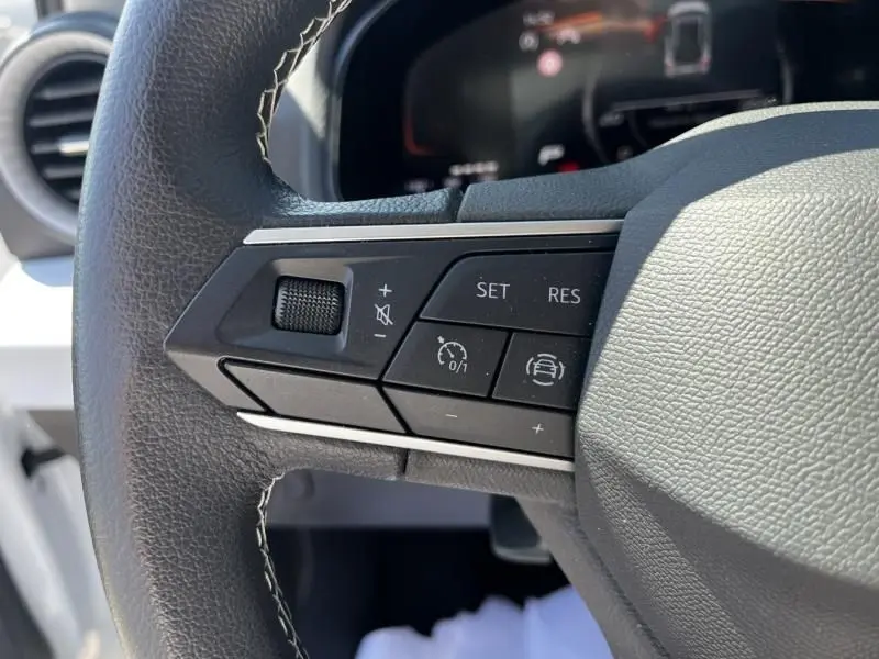 Gros plan sur les commandes de régulateur de vitesse au volant d’un SEAT Arona blanc 2024, côté gauche.