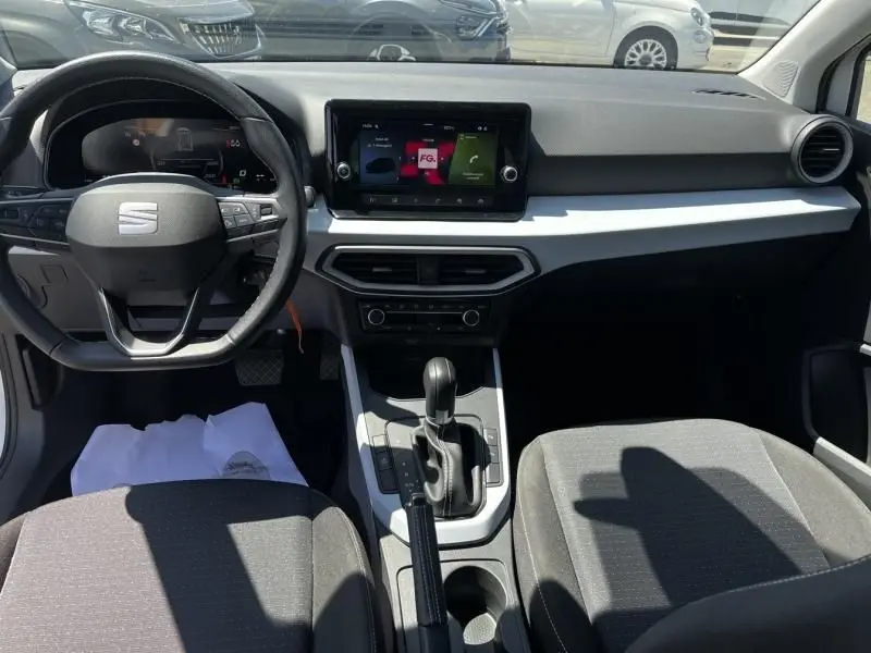 Vue intérieure avant du SEAT Arona blanc 2024, mettant en valeur le tableau de bord moderne et la console centrale avec boîte auto DSG7.