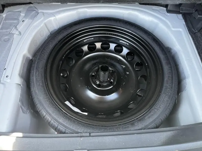 Roue de secours noire en acier vue de dessus dans le coffre d'un SEAT Arona blanc 2024 essence boîte auto.