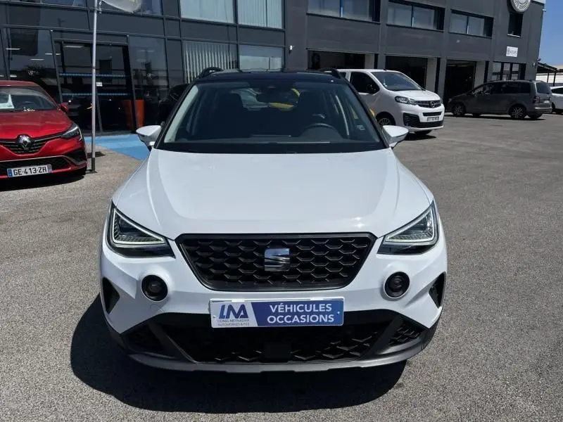 Vue frontale d'un SEAT Arona blanc 2024 avec calandre noire et phares LED anguleux sur un parking extérieur.