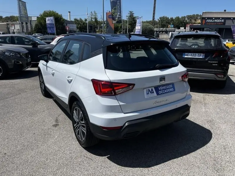 Vue 3/4 arrière droite d'un SEAT Arona blanc 2024 avec toit noir, en stationnement extérieur sur un parking.