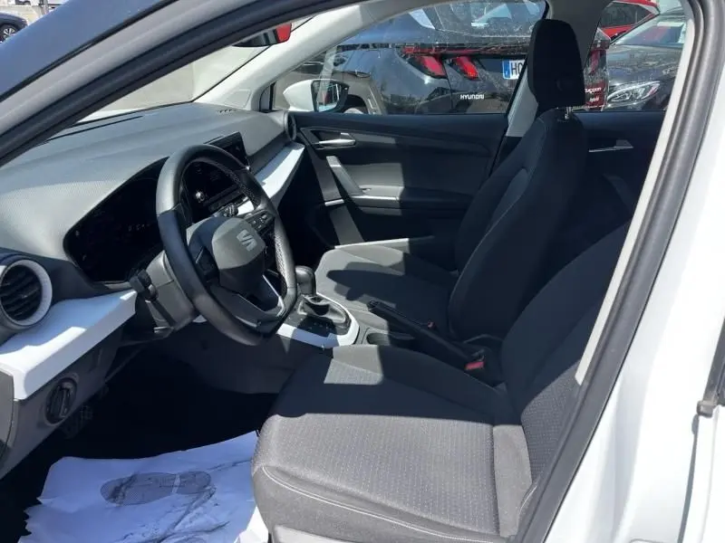 Vue intérieure côté conducteur du SEAT Arona blanc 2024, montrant le volant, tableau de bord et sièges noirs.