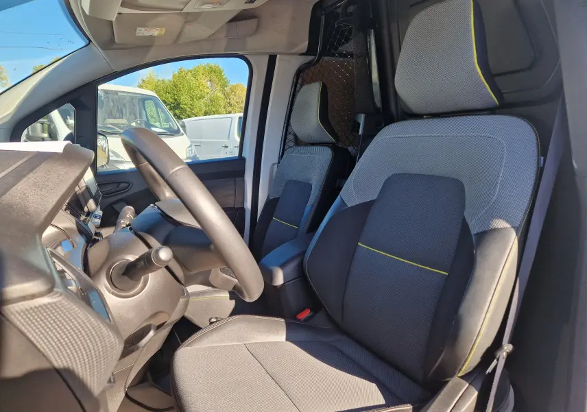 Vue intérieure côté conducteur du Renault Kangoo Van 2023, sièges gris avec surpiqûres jaunes et grille de séparation amovible.
