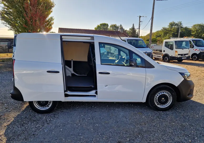 Vue latérale droite d’un Renault Kangoo blanc 2023 avec porte coulissante ouverte, montrant l’intérieur utilitaire et la grille de séparation.