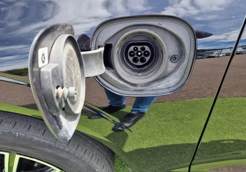 Prise de recharge ouverte côté gauche sur un Volvo XC60 noir, avec jante alliage visible en bas.