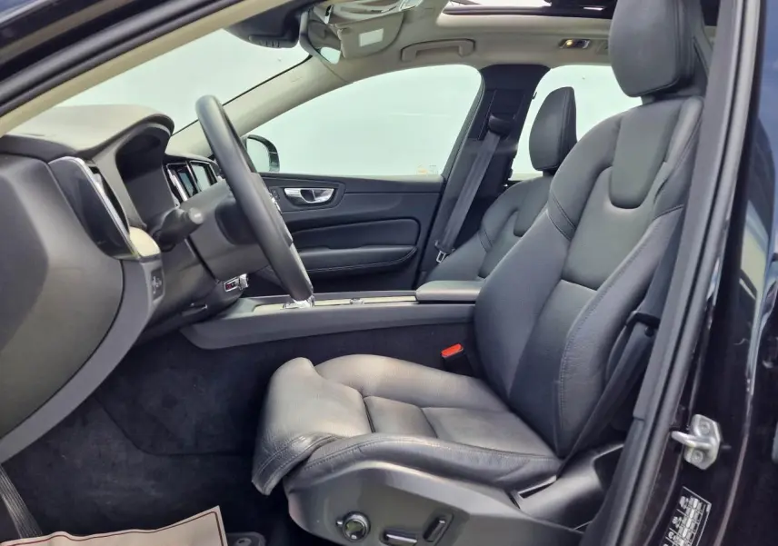 Intérieur côté conducteur du Volvo XC60 noir, sièges cuir confort avec réglages électriques et toit panoramique visible.