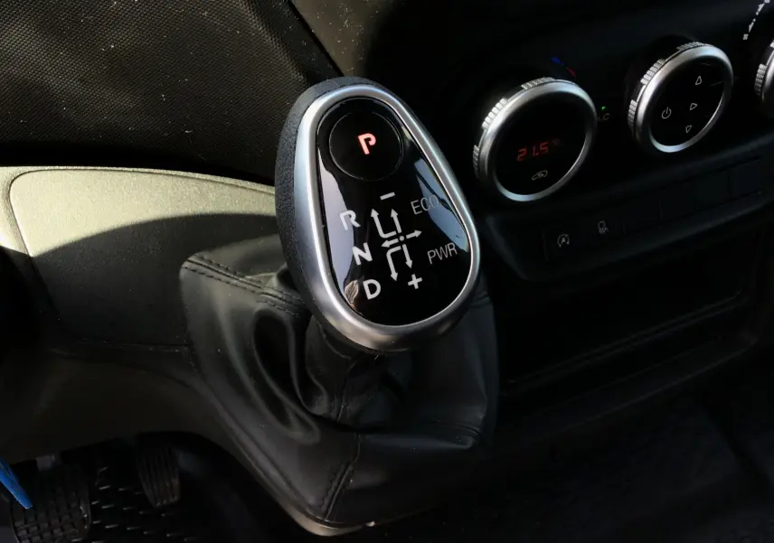 Gros plan sur le levier de vitesses automatique noir et argenté de l'Iveco Daily Fourgon blanc, avec commandes de climatisation en arrière-plan.