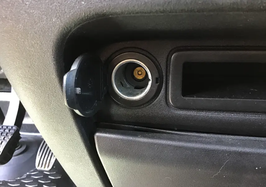 Prise allume-cigare ouverte dans l'habitacle noir du fourgon Iveco Daily blanc, vue rapprochée côté conducteur.