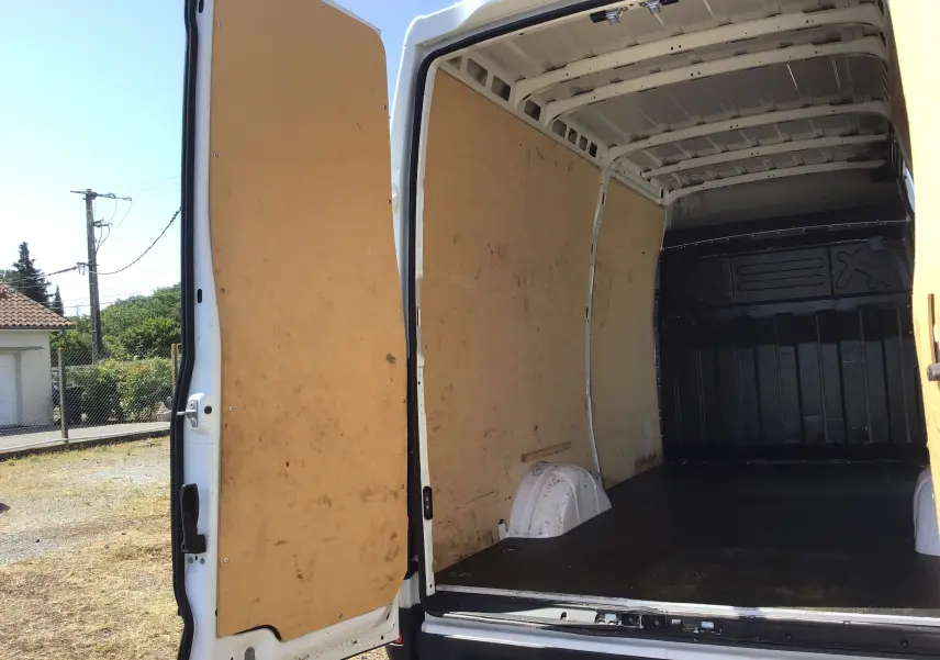 Vue arrière ouverte du fourgon blanc Iveco Daily 2022, montrant l'intérieur spacieux avec parois en bois et plancher noir.