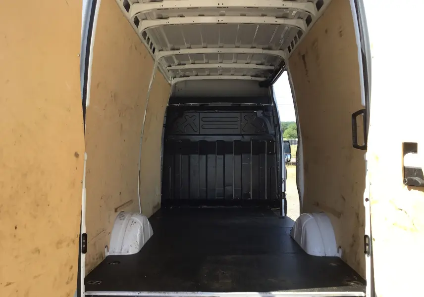 Vue intérieure arrière du fourgon Iveco Daily blanc 2022, montrant l'espace de chargement avec parois en bois et plancher noir.