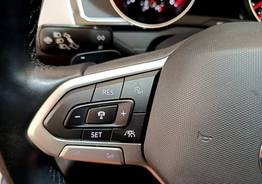 Gros plan sur le volant cuir de la Volkswagen Passat gris foncé, avec commandes de régulateur de vitesse et tableau de bord en arrière-plan.