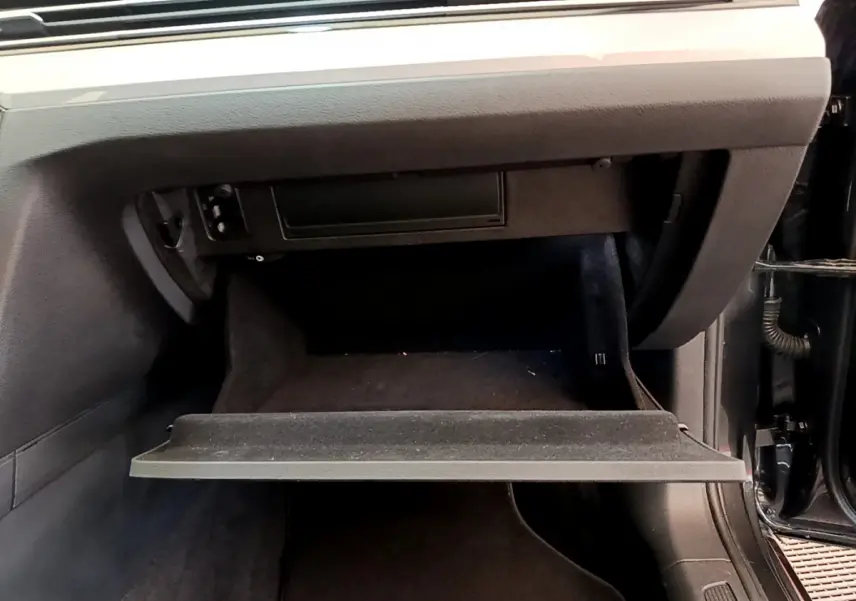 Gros plan sur la boîte à gants ouverte côté passager d'une Volkswagen Passat gris foncé, intérieur noir.