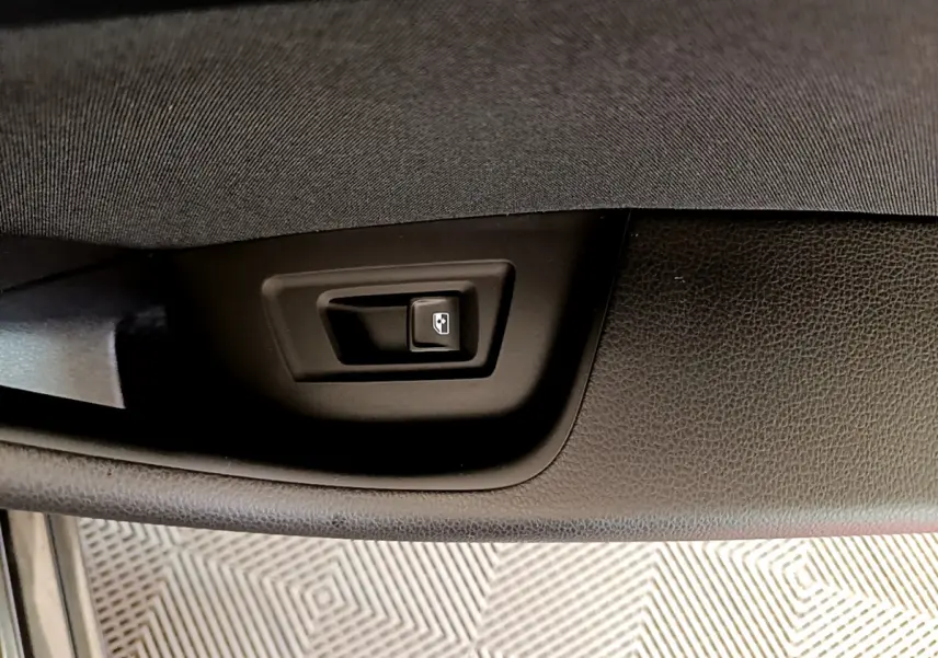 Gros plan sur le bouton d'ouverture du coffre intégré dans le panneau de porte noir d'une Volkswagen Passat gris foncé.