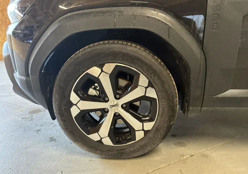 Gros plan sur la roue avant gauche du Dacia Duster noir 2025, mettant en valeur la jante au design moderne bicolore.