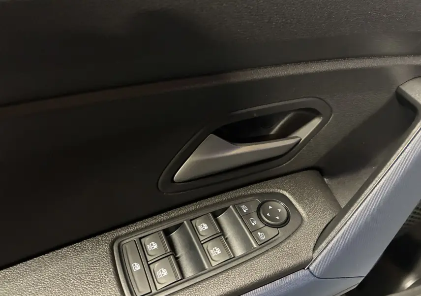Gros plan sur la commande des vitres électriques et la poignée intérieure côté gauche du Dacia Duster noir 2025.