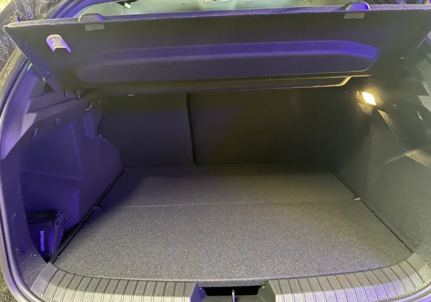 Coffre ouvert du Dacia Duster 1.6 Hybrid 140 Journey 2025 noir, vue intérieure montrant l'espace de chargement avec éclairage latéral.