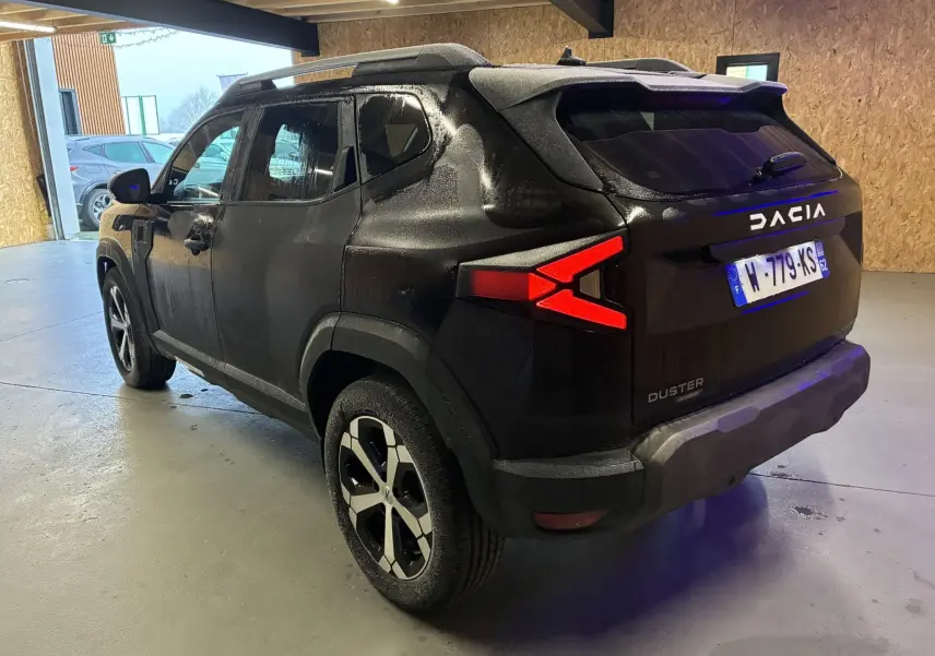 Vue 3/4 arrière droite d’un Dacia Duster noir 2025 avec feux arrière en forme de flèche et jantes bicolores.