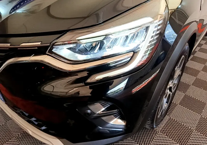 Gros plan sur l'avant droit noir brillant du Renault Captur 2021, mettant en valeur son phare LED et la calandre chromée.