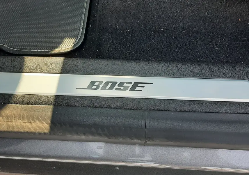 Gros plan sur la plaque de seuil de porte avec logo Bose, intérieur noir et carrosserie gris cassiopée du Renault Scénic IV.