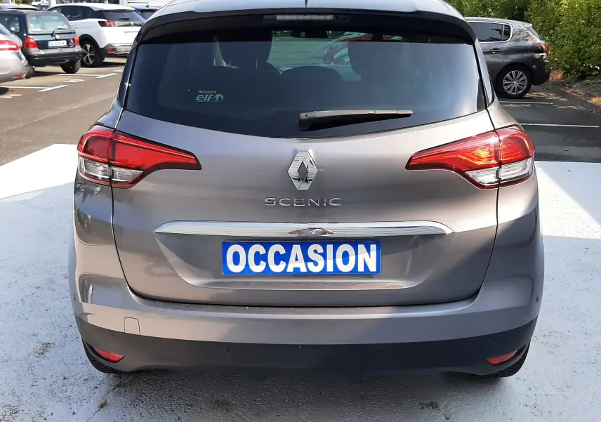 Vue arrière d'un Renault Scénic IV gris Cassiopée avec toit noir, plaque "OCCASION" visible sur un parking extérieur.