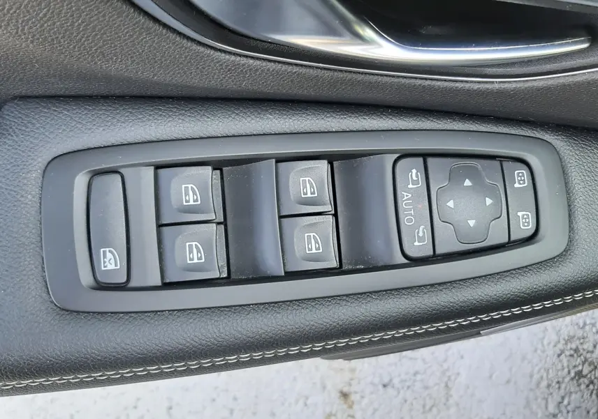Gros plan sur les commandes de lève-vitres et réglages des rétroviseurs sur la porte côté gauche du Renault Scénic IV gris Cassiopée.