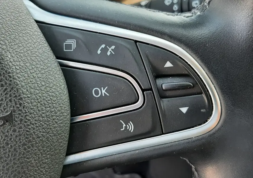 Gros plan sur les commandes multifonctions à gauche du volant en cuir noir du Renault Scénic IV gris Cassiopée.